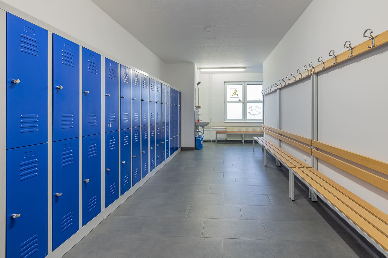 Umkleideraum mit blauen Spinden, Sitzbänken und Garderobenhaken